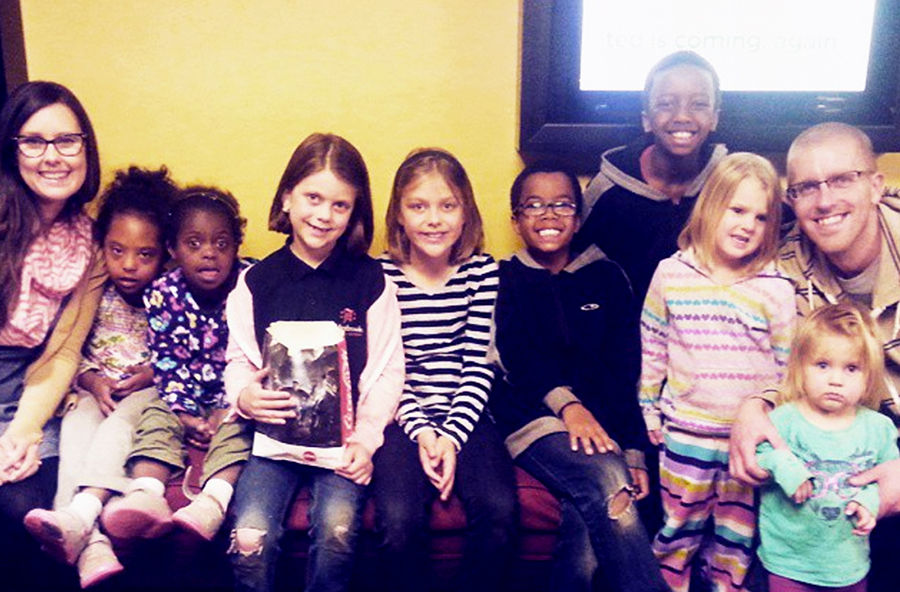 A group of diverse children sitting together against a yellow wall